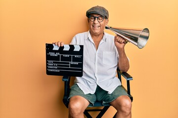 Canvas Print - Handsome mature director man holding video film clapboard and louder winking looking at the camera with sexy expression, cheerful and happy face.