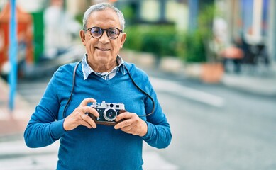 Wall Mural - senior grey-haired tourist man smiling happy using vintage camera at the city.