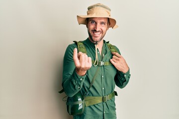 Poster - Handsome man with beard wearing explorer hat and backpack beckoning come here gesture with hand inviting welcoming happy and smiling