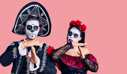 Poster - Young couple wearing mexican day of the dead costume over background doing time out gesture with hands, frustrated and serious face