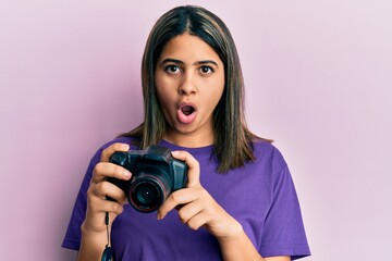 Poster - Young latin woman using reflex camera afraid and shocked with surprise and amazed expression, fear and excited face.