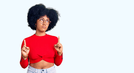 Poster - Young african american girl wearing casual clothes and glasses pointing up looking sad and upset, indicating direction with fingers, unhappy and depressed.