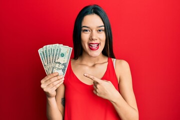 Poster - Young hispanic girl holding 20 dollars banknote smiling happy pointing with hand and finger