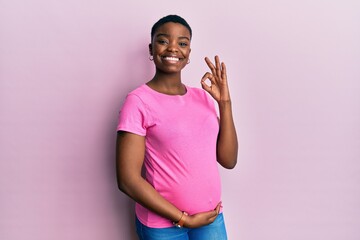 Sticker - Young african american woman expecting a baby, touching pregnant belly smiling positive doing ok sign with hand and fingers. successful expression.