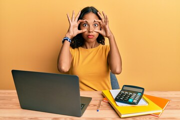 Poster - Young african american girl working at the office with laptop and calculator trying to open eyes with fingers, sleepy and tired for morning fatigue