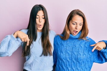 Poster - Hispanic family of mother and daughter wearing wool winter sweater pointing down with fingers showing advertisement, surprised face and open mouth