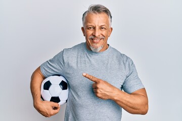 Canvas Print - Middle age grey-haired man holding soccer ball smiling happy pointing with hand and finger