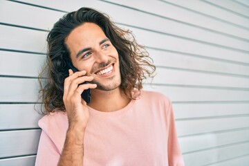 Young hispanic man smiling happy talking on the smartphone leaning on the wall