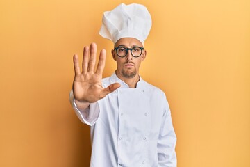 Bald man with beard wearing professional cook uniform doing stop sing with palm of the hand. warning expression with negative and serious gesture on the face.