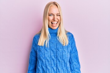 Canvas Print - Young blonde girl wearing wool winter sweater winking looking at the camera with sexy expression, cheerful and happy face.