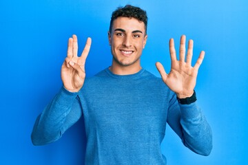 Hispanic young man wearing casual winter sweater showing and pointing up with fingers number eight while smiling confident and happy.