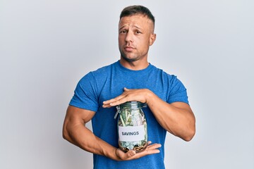 Sticker - Handsome muscle man holding jar with savings clueless and confused expression. doubt concept.