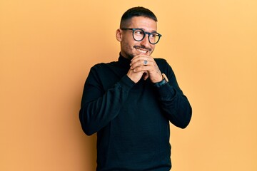 Poster - Handsome man with tattoos wearing turtleneck sweater and glasses laughing nervous and excited with hands on chin looking to the side