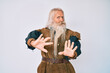 Old senior man with grey hair and long beard wearing viking traditional costume afraid and terrified with fear expression stop gesture with hands, shouting in shock. panic concept.