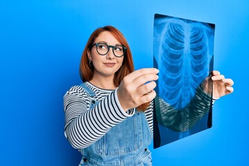 Poster - Beautiful redhead woman holding chest radiography smiling looking to the side and staring away thinking.