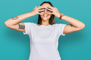 Young hispanic woman wearing casual white t shirt covering eyes with hands smiling cheerful and funny. blind concept.