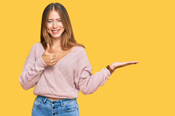 Beautiful blonde woman wearing casual winter pink sweater showing palm hand and doing ok gesture with thumbs up, smiling happy and cheerful