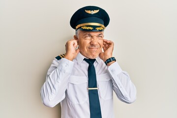 Poster - Handsome middle age mature man wearing airplane pilot uniform covering ears with fingers with annoyed expression for the noise of loud music. deaf concept.