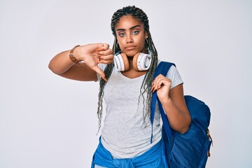 Sticker - Young african american woman with braids wearing student backpack and headphones with angry face, negative sign showing dislike with thumbs down, rejection concept