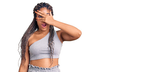 Poster - Young african american woman with braids wearing sportswear peeking in shock covering face and eyes with hand, looking through fingers with embarrassed expression.