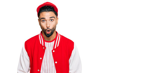 Wall Mural - Young man with beard wearing baseball uniform afraid and shocked with surprise expression, fear and excited face.