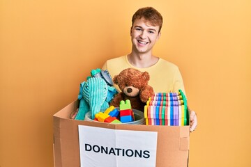 Young caucasian man holding donation box with toys smiling with a happy and cool smile on face. showing teeth.