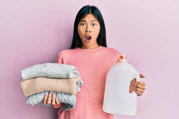 Sticker - Young chinese woman holding detergent bottle and clothes afraid and shocked with surprise and amazed expression, fear and excited face.