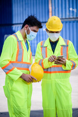 Engineer men wearing yellow hardhat standing near forklift cargo at the container yard and check for control loading Containers box from Cargo freight ship for import and export. Teamwork concept