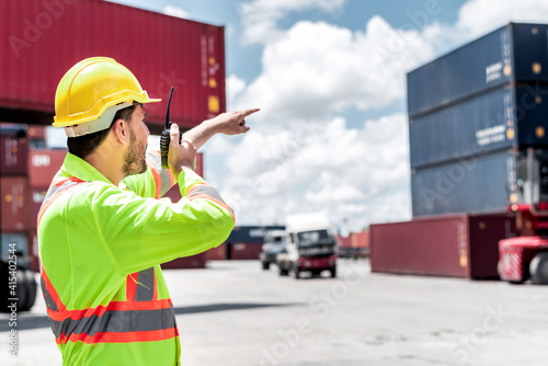 Confident Caucasian man engineer wearing yellow safety helmet using walkies talkie call to driver and check for control loading containers box from Cargo freight ship for import and export, transport © totojang1977
