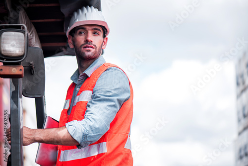 Young confident Caucasian man engineer driving Forklift and wearing white safety helmet and check for control loading containers box from Cargo freight ship for import and export, transport © totojang1977