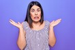 © Krakenimages.com - Young beautiful brunette woman wearing casual striped t-shirt standing over purple background clueless and confused with open arms, no idea and doubtful face.