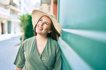 Wall Mural - Young hispanic woman on vacation smiling happy leaning on the wall at street of city