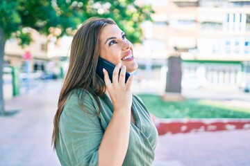 Wall Mural - Young hispanic woman smiling happy talking on the smartphone walking at street of city