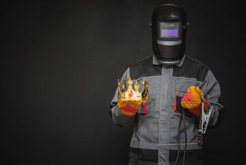 Welder man in the helmet with a welding terminals is holding in the hand a golden crown on the black background. Best welder concept.