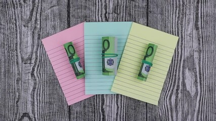 Fototapete - Rolls of 100 Euro banknotes on colored notepads arranged fanned to the centre of the screen on a wood background in an overhead view for financial concepts. Stop motion, top view