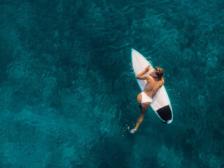 Wall Mural - Attractive surfer woman relaxing on surfboard in ocean. Aerial view with surf girl