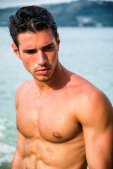 Wall Mural - Attractive young man in the sea getting out of water with wet hair, looking away to a side