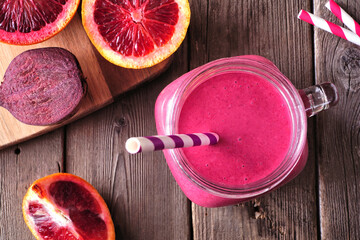 Wall Mural - Smoothie with red oranges and beets in a mason jar glass. Close up top view table scene on a rustic wood background.