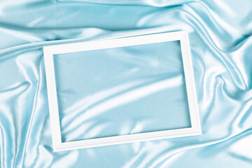 Wall Mural - Empty white wooden frame on beautiful light blue silk satin background. Top view
