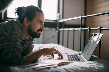 Young man lies on bed with laptop at home