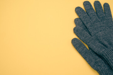 Closeup shot of gray knitted pair of gloves on a yellow background