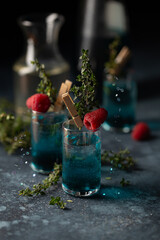 Wall Mural - Set of cocktails in shot glasses with blue liqueur,thyme sprigs and fresh raspberry.Close up of blue drink.