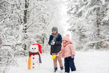 Cute Boy And Girl Building Snowman In Winter Forest