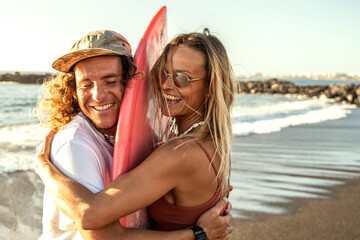 Wall Mural - Happy surfer couple with surfboard having fun on the beach, smiling, spending time together. Sporty people. Real people emotions. Extreme surfing sport and youth relationship lifestyle concept