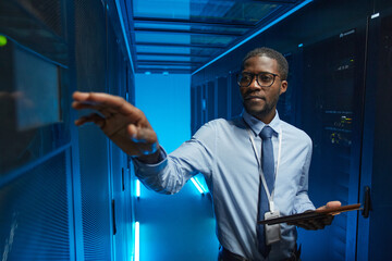 Wall Mural - Waist up portrait of African American man reaching for server cabinet while working with supercomputer in data center and holding tablet, copy space