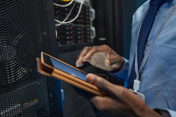 Wall Mural - Close up of African American man holding digital tablet while standing by server cabinet and working with supercomputer in data center, copy space
