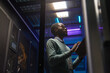 © Seventyfour - Low angle portrait of African American data engineer working with supercomputer in server room lit by blue light, copy space