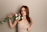 Fototapeta Tulipany - Happy woman with a bouquet of light flowers on a beige background naked shoulders model red hair beautiful face