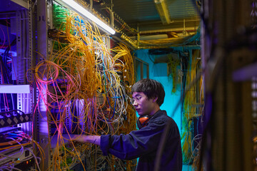 Wall Mural - Side view portrait of young network technician connecting cables in server room, copy space