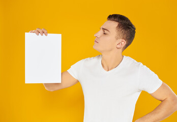 Guy with a white sheet of paper on a yellow background blank business card advertising